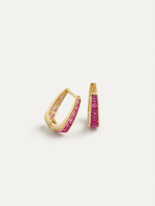 A pair of gold huggie hoop earrings with a channel-set row of pink gemstones on a clean white background.