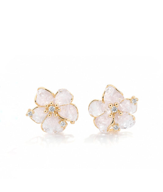 A pair of gold flower-shaped stud earrings featuring pale pinkish-white raw stone petals and small clear crystal accents in the center, set against a clean white background.