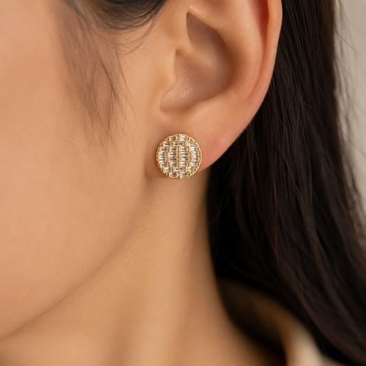 Round gold-toned stud earring with clear baguette-cut crystals worn on a woman's ear.
