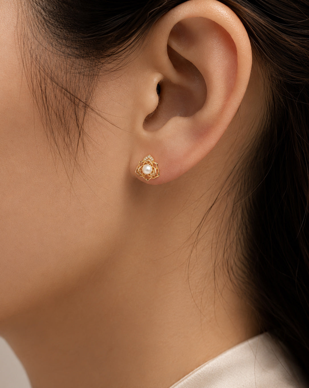 Close-up of a woman wearing a gold-tone floral stud earring with a central pearl.