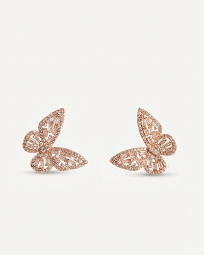A pair of rose gold butterfly-shaped stud earrings embellished with clear baguette and round crystals, set against a plain white background.