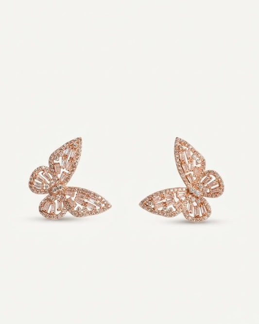 A pair of rose gold butterfly-shaped stud earrings embellished with clear baguette and round crystals, set against a plain white background.