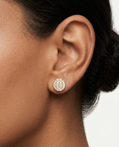 Close-up of a woman wearing a circular rose gold stud earring with a radial baguette-cut stone pattern.
