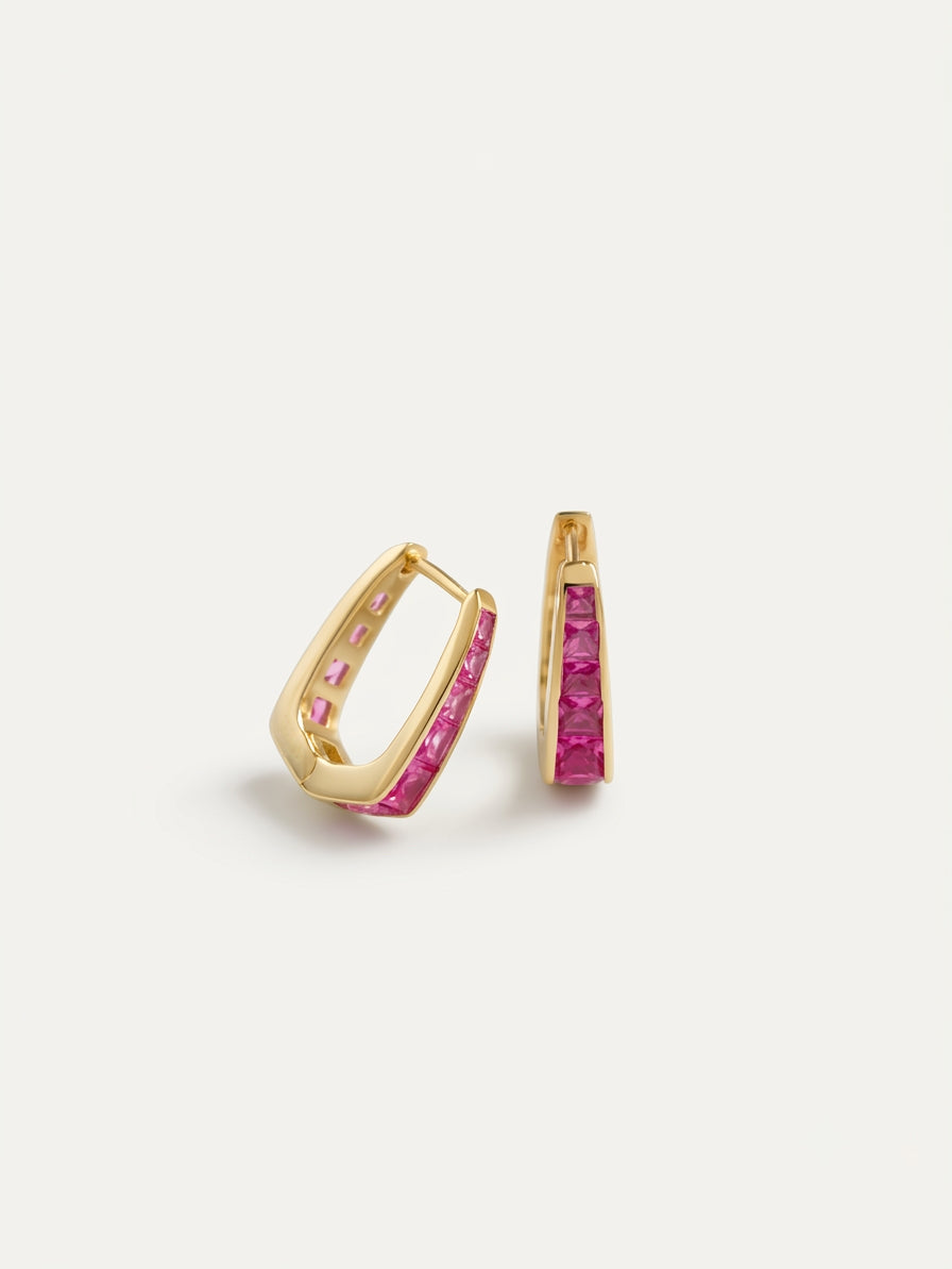 A pair of gold huggie hoop earrings with a channel-set row of pink gemstones on a clean white background.