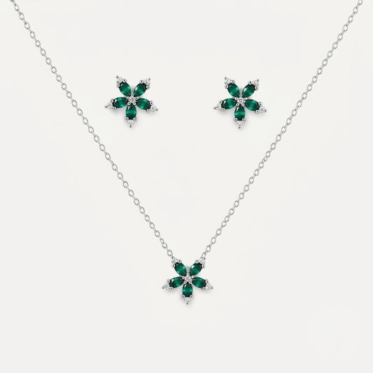 A silver jewelry set featuring a delicate chain necklace and matching stud earrings, each adorned with a five-petal flower design in polished green stones and small clear accent stones, set against a light gray background.