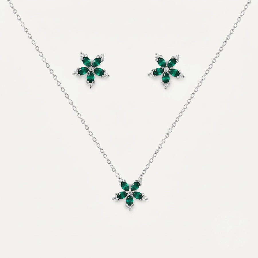 A silver jewelry set featuring a delicate chain necklace and matching stud earrings, each adorned with a five-petal flower design in polished green stones and small clear accent stones, set against a light gray background.