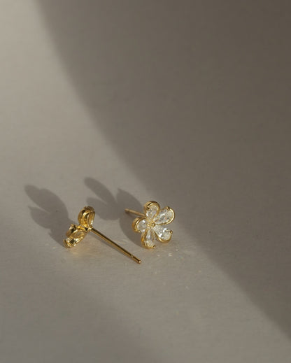 Gold-tone flower-shaped stud earrings with clear stones on grey background 