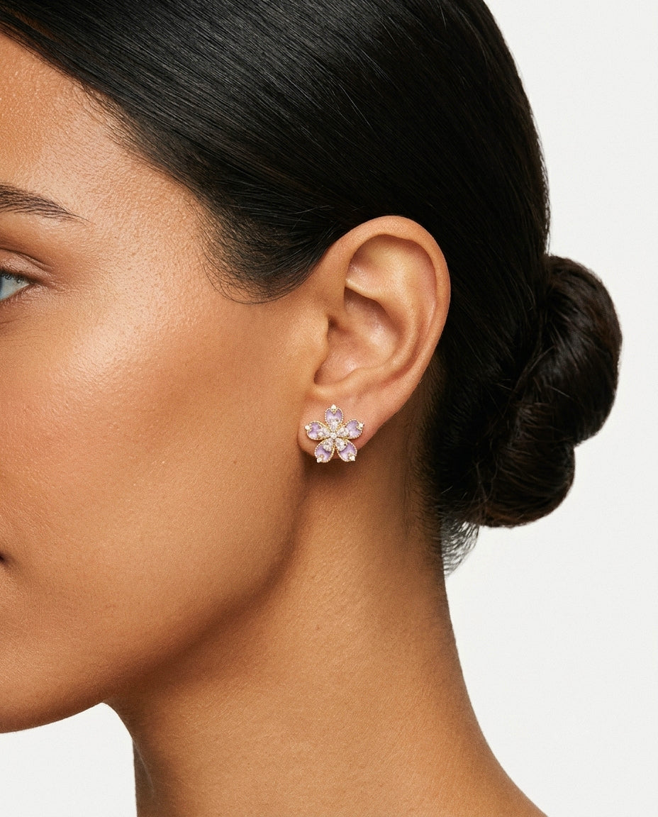Close up of wearing a flower-shaped stud earrings with purple enamel petals and clear stone accents.