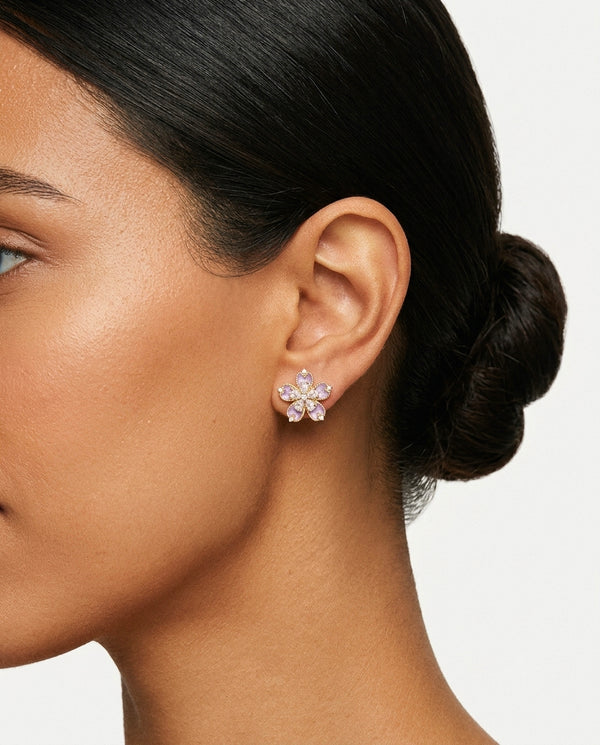 Close up of wearing a flower-shaped stud earrings with purple enamel petals and clear stone accents.