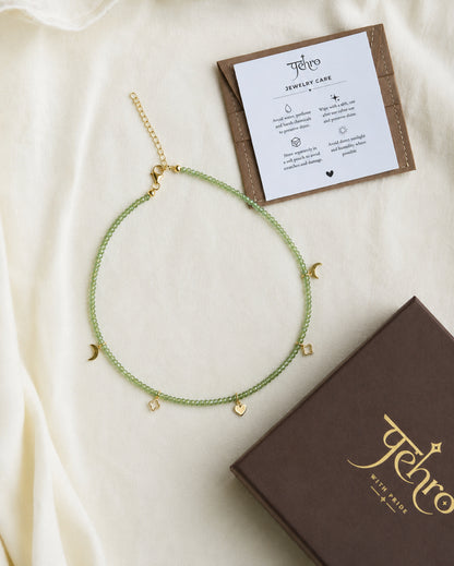 PEHRO peridot gemstone choker with faceted green peridot beads and gold-tone charms, presented with its jewellery box and care card.
