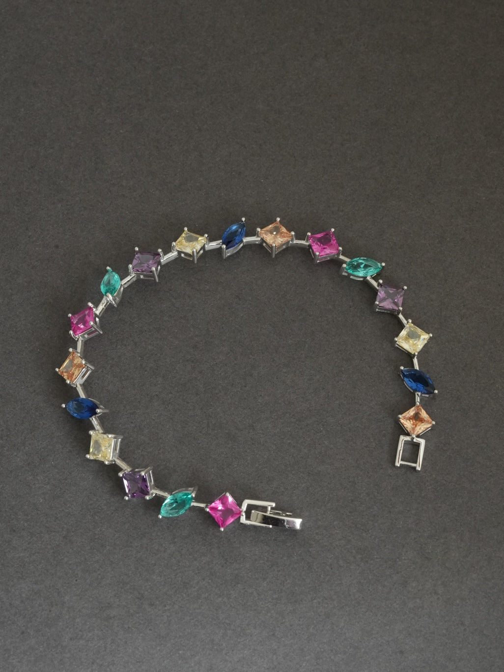 The 925 Sterling Silver Multicolor Station Bracelet draped over a minimal sculptural form, highlighting its lightweight construction and rhodium finish. On a dark gray background 