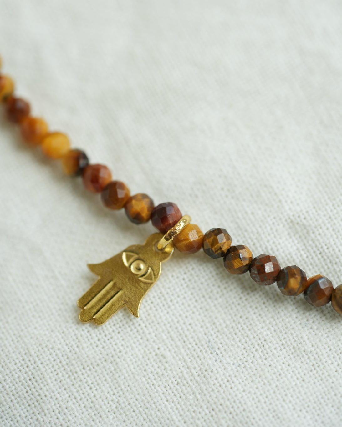 Natural Tiger Eye beaded charm necklace with five 18K gold charms, including hand, flower and heart motifs.