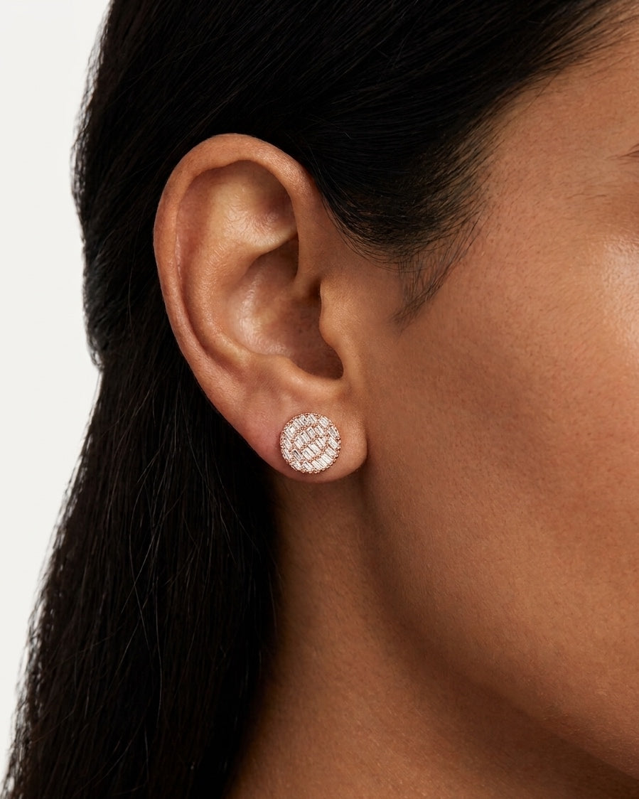 Close-up of a woman wearing a circular rose gold stud earring with a radial baguette-cut stone pattern.