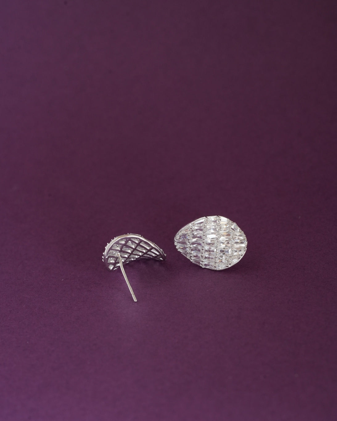 Pair of silver-tone teardrop-shaped stud earrings with baguette-cut clear stones on a dark purple background