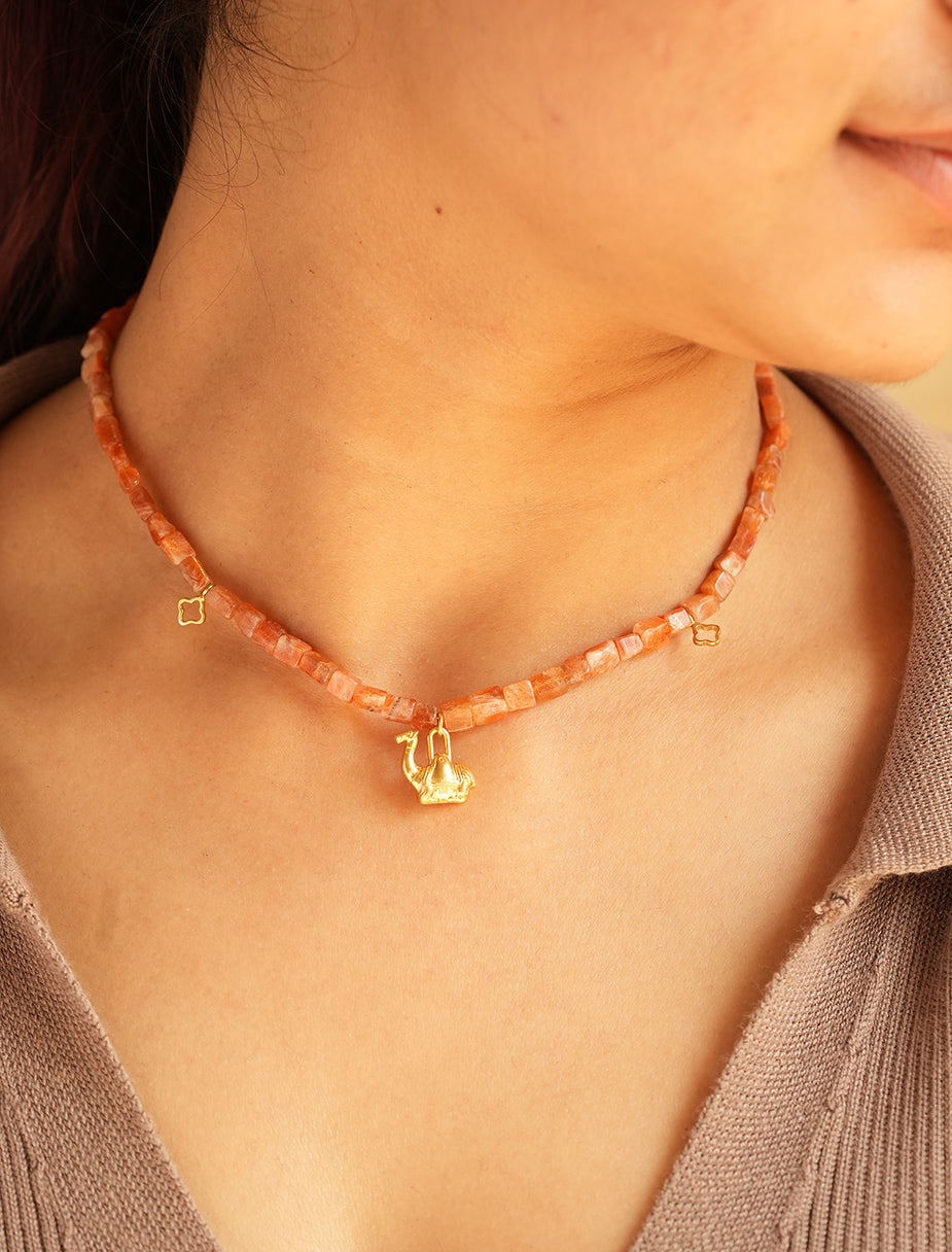 Close-up of PEHRO sunstone choker worn at the collarbone, warm peach-orange faceted beads with a small gold camel charm