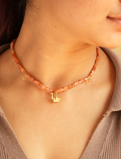 Close-up of PEHRO sunstone choker worn at the collarbone, warm peach-orange faceted beads with a small gold camel charm