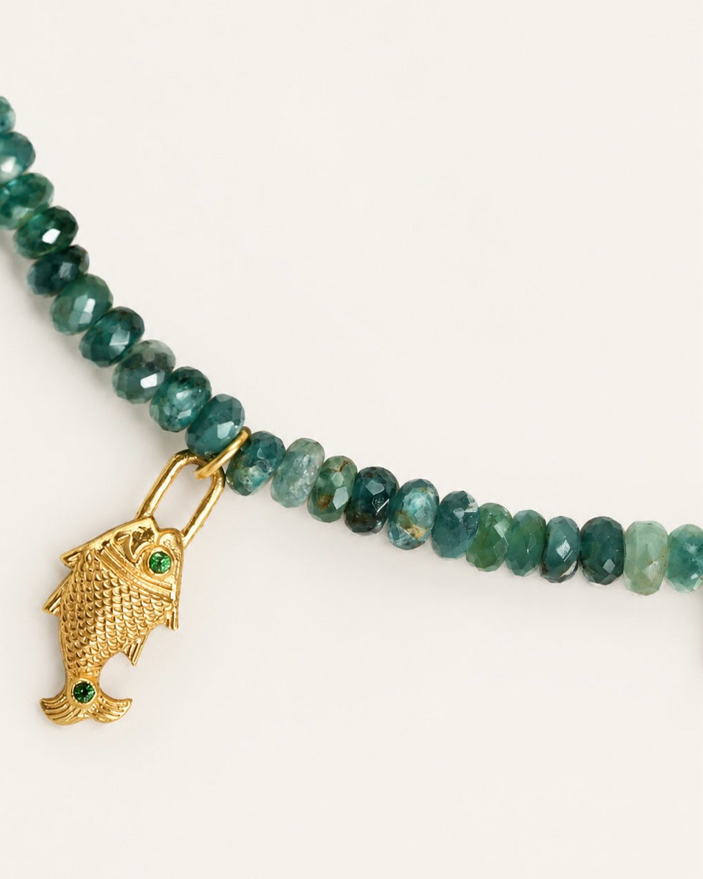 Close-up of a natural grandidierite gemstone choker with faceted green-blue beads and a gold fish charm with green stone details.