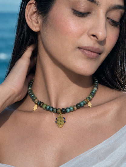 A woman elegantly styling the PEHRO gold vermeil chrysocolla beaded choker over a white silk drape, highlighting how the natural stones rest beautifully on the collarbone.
