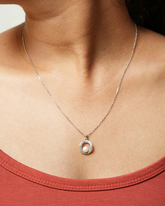 Woman wearing a silver necklace with a circular sparkling pendant and a central white pearl.