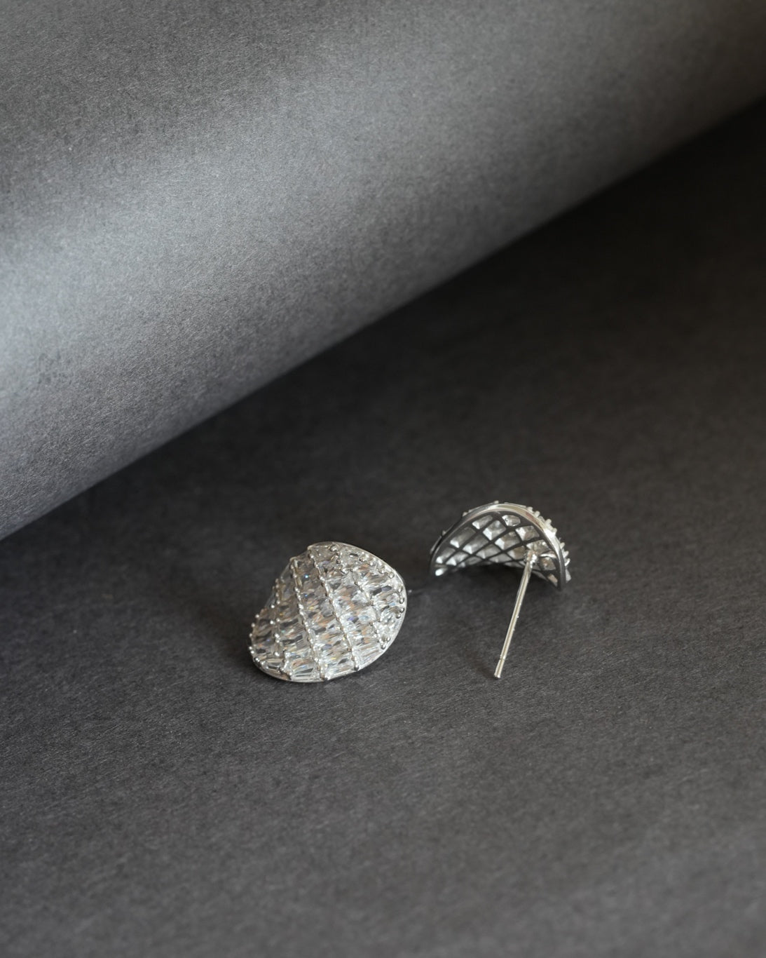 Pair of silver-tone teardrop-shaped stud earrings with baguette-cut clear stones on a dark gray background