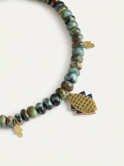 Macro detail of the textured 18K gold vermeil fish pendant and hamsa charms resting against natural blue, green, and brown chrysocolla gemstone beads.