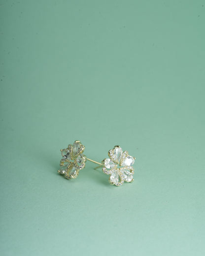 A pair of gold flower-shaped stud earrings with clear rhinestones, displayed on a solid mint green background.