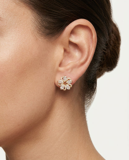 A close-up of a model's ear wearing a small flower-shaped stud earring with clear stones and a gold center.