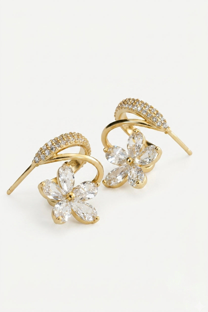 A pair of gold-toned drop earrings featuring a curved bar set with small clear crystals and a dangling flower-shaped crystal cluster at the bottom, shown on a plain white background.