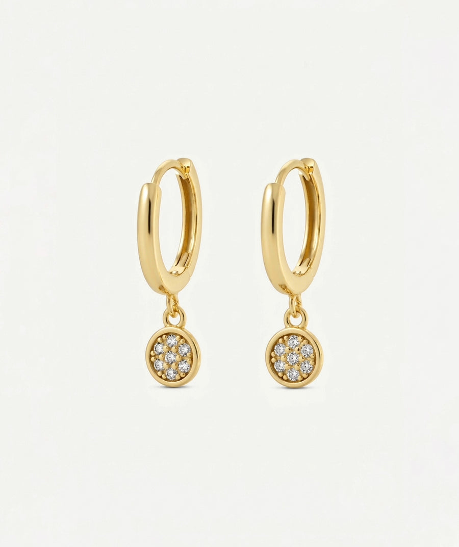 A pair of gold huggie hoop earrings with small circular pavé dangle charms set with clear stones, shown on a clean white background.