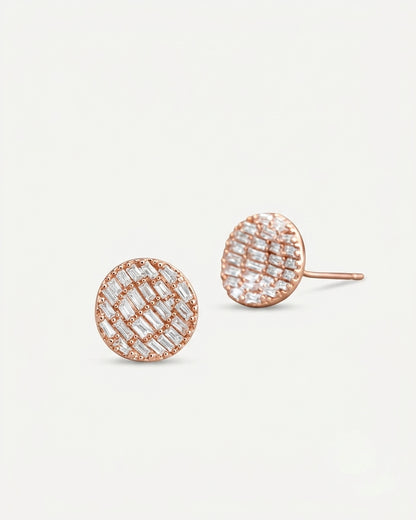 A pair of round rose gold stud earrings with a textured grid pattern of clear baguette and round-cut stones, shown on a clean off-white background.